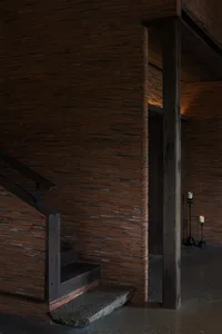 A dimly lit interior staircase in a brick building with a wooden staircase and brick walls