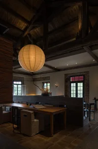 A modern restaurant interior with wooden walls and floors, featuring dining tables and chairs, potted plants, and a welcoming atmosphere