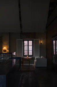 Cozy living room with a couch, table, chair, and potted plants, lit by natural light from a window