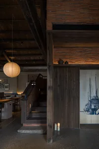 A warm and inviting hotel lobby with wooden walls and floors, featuring two staircases and multiple chairs, creating a cozy and comfortable atmosphere