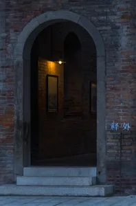 Dimly lit hallway with a brick wall, two framed pictures, and an archway leading to a dark space