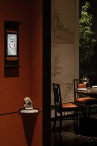 Cozy Asian restaurant dining area with wooden chairs and a table set for a meal, surrounded by a potted plant and warm atmosphere