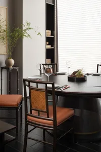 Dining area with a large wooden table, multiple chairs, wine glasses, utensils, and books, set up for a meal or gathering in a sophisticated setting