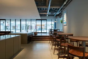 Modern restaurant interior with a large dining area, tables, chairs, and potted plants