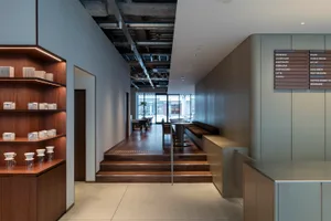 A modern lobby with wooden floors and walls, featuring chairs and a potted plant, with a well-designed atmosphere