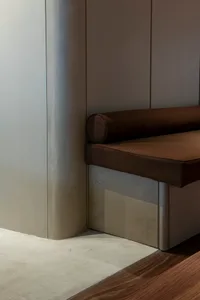 A modern and minimalist interior design featuring a wooden bench and metal accents against a silver wall, with natural light pouring in from a large window