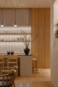 A rustic kitchen with wooden walls and floors, featuring two dining tables and multiple chairs, with decorative vases scattered throughout the space