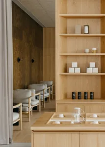 A modern interior design showroom with wooden walls and floors, featuring two couches, three chairs, and decorative bottles, creating a clean and inviting atmosphere
