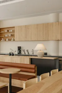 A modern kitchen and dining area with wooden floors and cabinets, featuring a dining table, couches, a chair, and kitchen appliances