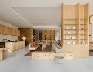 Open living area with wooden floors and walls, featuring a sink, chairs, and a potted plant, with a modern and spacious design