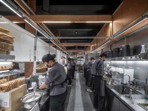 熱鬧的商業廚房有多人忙著準備食物，配備現代家電、烤箱和散落的瓶子，營造出忙碌動感的氛圍