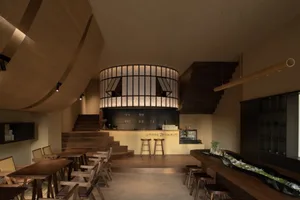Warm and inviting restaurant interior with wooden floors, tables, chairs, and a bar area, featuring multiple dining tables and comfortable seating