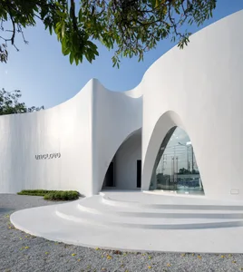 Modern building with a white facade, a curved wall, and glass doors, set in a clean and minimalist environment
