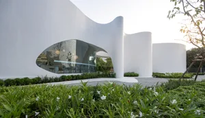 Contemporary museum space with a curved design, a large glass wall, and natural light, featuring chairs and a sophisticated atmosphere