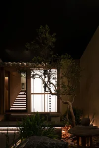 A calm and inviting interior space with a wooden staircase, metal railing, and a tree in the center, surrounded by walls and a floor