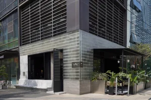 Sleek modern building with a black facade, gray stone-like material, and a large glass wall, surrounded by potted plants