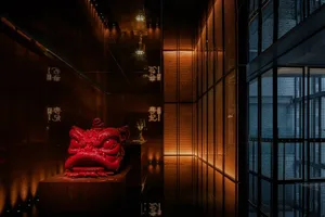 A dimly lit room with a wooden table, chairs, and an ornate red dragon statue as a centerpiece