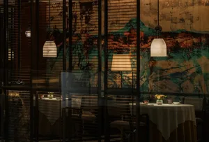 A modern dining area with two tables, chairs, and a large painting on the wall, creating a comfortable atmosphere for guests