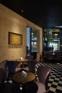 A modern restaurant with a large dining table and several smaller tables, purple accents, and a concrete finish, lit by lamps creating a warm ambiance