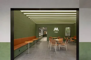 A modern restaurant interior with green walls, wooden flooring, and multiple dining tables and benches