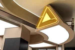 A modern interior space with a large yellow wooden triangle on the ceiling, surrounded by functional and aesthetically pleasing design elements