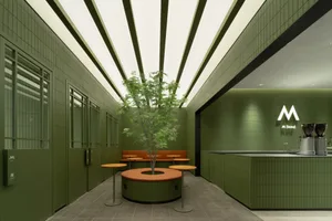 A restaurant interior with green walls, a large tree in a pot, and dining tables with chairs, creating a welcoming atmosphere with a focus on nature and greenery
