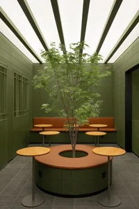 A cozy restaurant space with a large tree in a pot surrounded by dining tables and benches, with a warm and inviting atmosphere