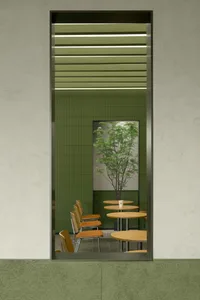 A restaurant interior with green walls, dining tables, chairs, and a potted plant, creating a cozy atmosphere for guests
