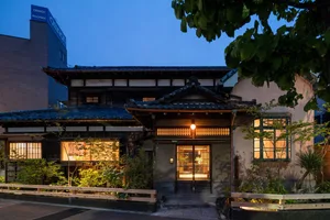 Exterior photo of an Asian-style house with a mix of traditional and modern elements, featuring a prominent wooden doorway and a warm inviting atmosphere