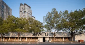 A modern building with a gray exterior, glass windows, and a large sign, surrounded by trees and a contemporary urban environment