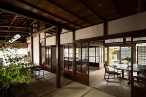 Warm and inviting living area with wooden floors and walls, featuring traditional Asian design elements, chairs, dining tables, and potted plants