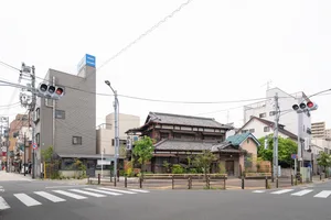 A tranquil Asian-style building with a large roof, surrounded by trees and bushes, featuring a mix of traditional and modern elements, including a clock mounted on its side, in a pedestrian-friendly zone