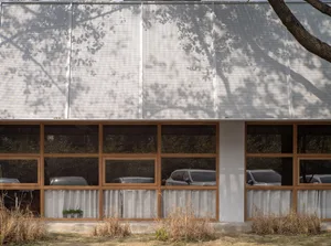 一座現代建築，擁有白色牆面與木質元素、多扇窗戶及簡潔設計，門前停有兩輛車
