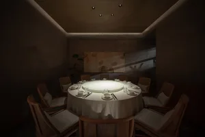 Formal dining area with a round table, wooden chairs, and wine glasses, set for a meal or event