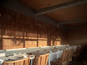 Empty restaurant dining area with wooden tables and chairs, bowls, cups, and spoons, clean and well-organized space for socializing and meals