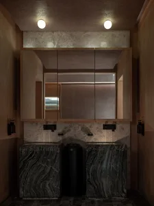 Bathroom with two sinks, a mirror, and a toilet, featuring a wooden design and dim lighting
