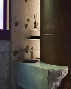 Modern bathroom with a sink basin in a concrete countertop, two bottles on the counter, and dim lighting