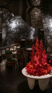 A warm and inviting dining area with a large red tree centerpiece on a table surrounded by chairs, creating a cozy atmosphere in the restaurant