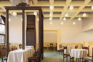 Dining area with multiple tables and chairs, warm tones on the walls, mixed flooring, and potted plants