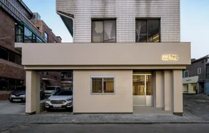 A modern building with a white exterior and a brick facade, featuring two cars and three people standing nearby