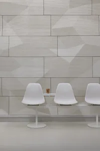Modern dining area with two white chairs and a small table in front of a wall with a unique brick pattern design
