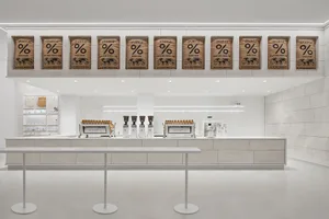 Industrial kitchen with white walls and floors, featuring coffee machines and cups, with a focus on functionality and efficiency