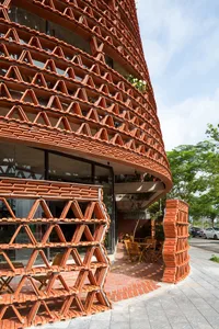 A modern building with a curved shape and brick facade, featuring a dining area with chairs and tables inside