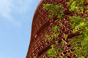 A modern building with a red brick exterior, multiple windows, and a natural setting with trees nearby