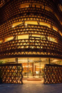 A modern building with a large wooden structure in front, featuring a seating area with chairs and potted plants both inside and outside