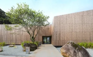 A wooden cabin with a large tree in front, surrounded by natural scenery, with a calm and serene atmosphere