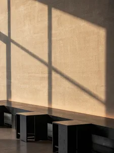 A dimly lit room with a cement wall, a window, and three wooden benches placed along the wall