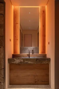 Bathroom with a sink under a mirror, stone wall, and wooden countertop, illuminated by lights