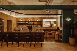 A bar area with wooden floors and walls, featuring a bar counter with seating and bottles on display, set in a warm and inviting atmosphere