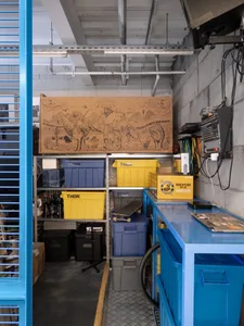 A cluttered industrial workshop with suitcases, crates, and bins scattered throughout, featuring various bottles and a disorganized atmosphere